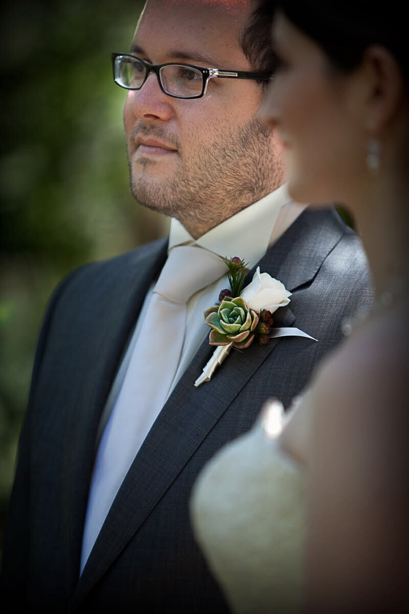 Groom wearing ivory tie and boutonniere with white rose and maroon and light green accents during ceremony - photo by South Africa based wedding photographer Greg Lumley